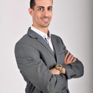 Businessman in a grey suit posing confidently with arms crossed against a neutral background.