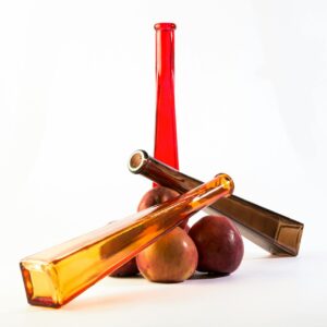Artistic arrangement of colorful glass bottles and red apples on a white background.