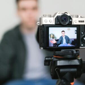 Man recording a vlog indoors using a mirrorless camera on a tripod with selective focus.